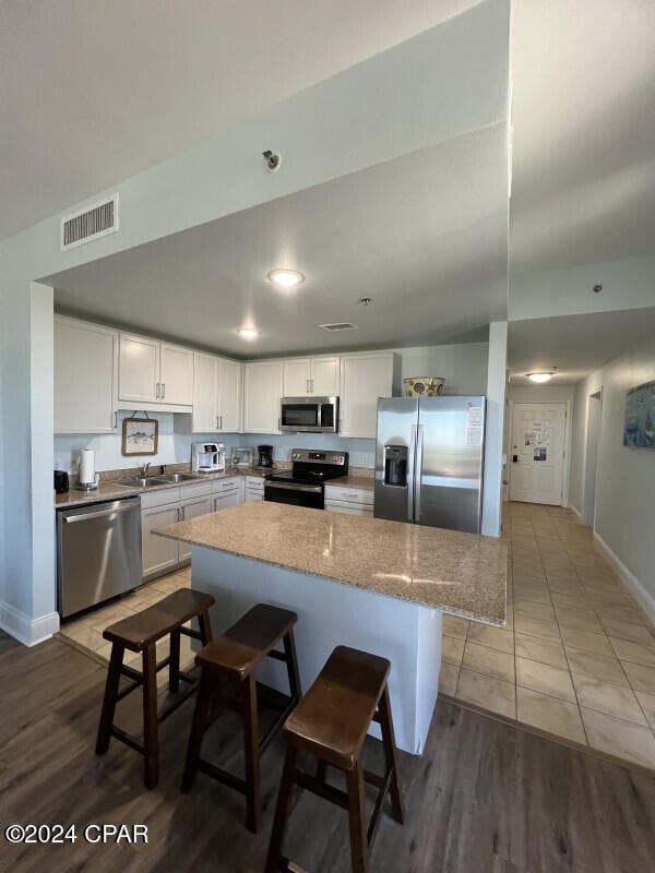 kitchen featuring a kitchen bar, sink, white cabinetry, stainless steel appliances, and light stone countertops