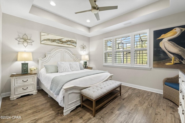 bedroom with a tray ceiling, ceiling fan, and dark wood-type flooring