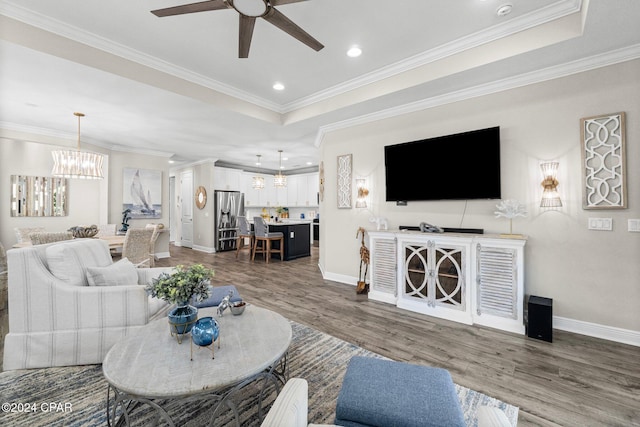 living room with hardwood / wood-style flooring, ceiling fan with notable chandelier, crown molding, and a tray ceiling