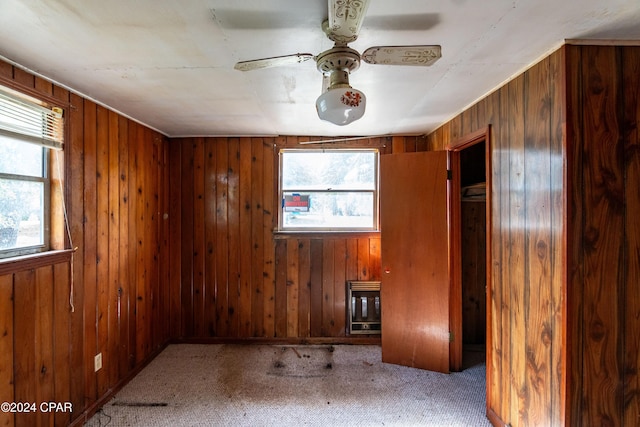 carpeted empty room featuring wood walls, ceiling fan, and heating unit