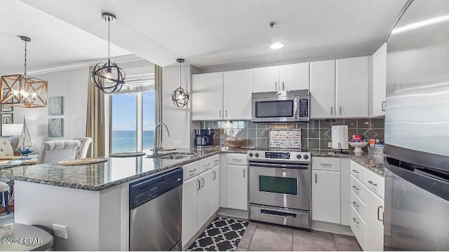 kitchen with stainless steel appliances, sink, decorative light fixtures, white cabinetry, and a water view