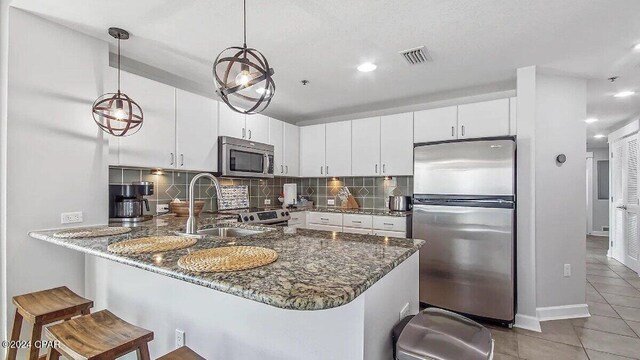 kitchen with appliances with stainless steel finishes, kitchen peninsula, white cabinets, and pendant lighting