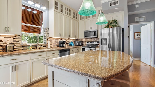 kitchen with light stone countertops, crown molding, appliances with stainless steel finishes, and a center island