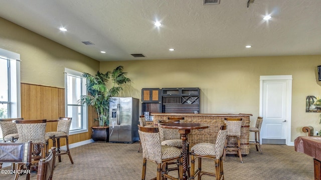 carpeted dining area featuring wood walls and a textured ceiling