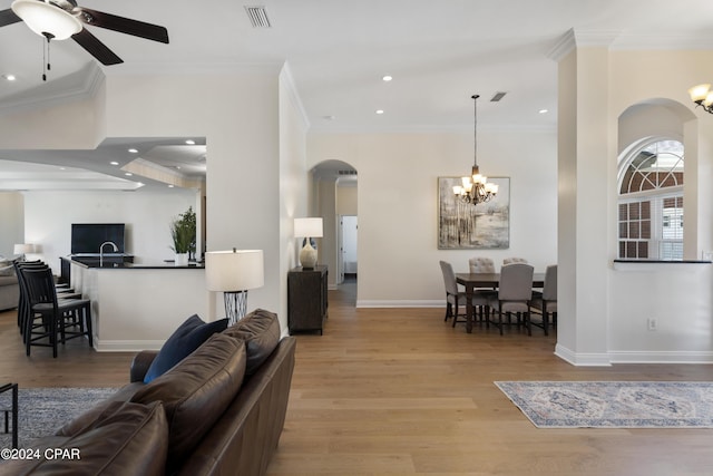 living room with ceiling fan with notable chandelier, light hardwood / wood-style floors, and crown molding