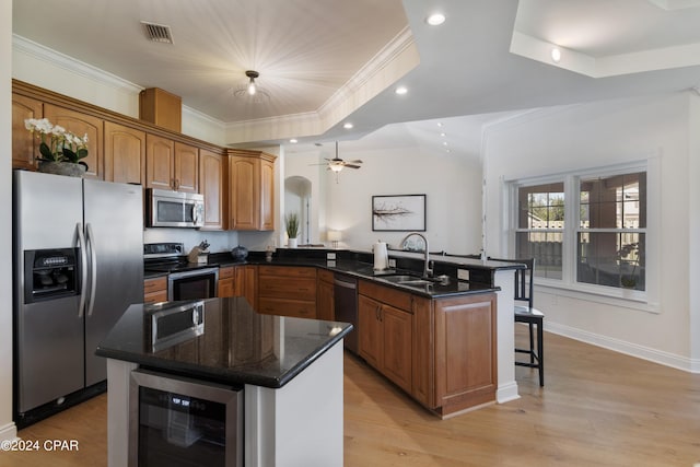 kitchen with wine cooler, a kitchen island with sink, sink, and appliances with stainless steel finishes