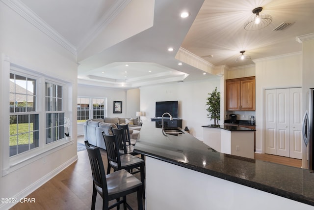 kitchen featuring sink, dark wood-type flooring, crown molding, dark stone counters, and a tray ceiling