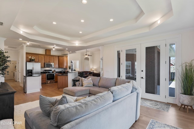 living room featuring french doors, a tray ceiling, ceiling fan, crown molding, and light hardwood / wood-style flooring