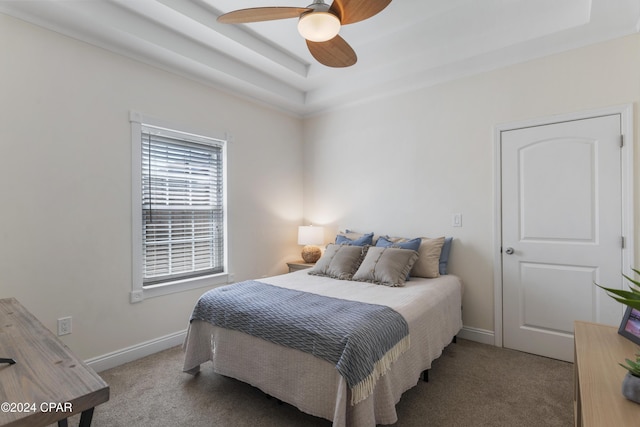 carpeted bedroom with a raised ceiling and ceiling fan