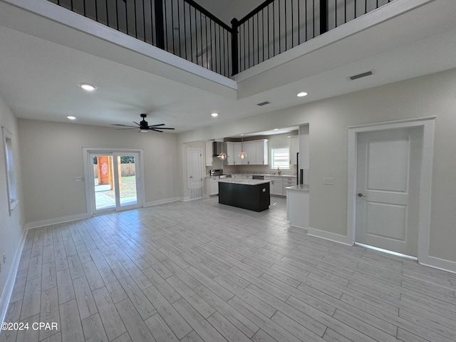 unfurnished living room with light hardwood / wood-style floors, a towering ceiling, and ceiling fan