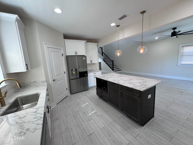 kitchen featuring stainless steel fridge, hanging light fixtures, white cabinetry, sink, and a center island