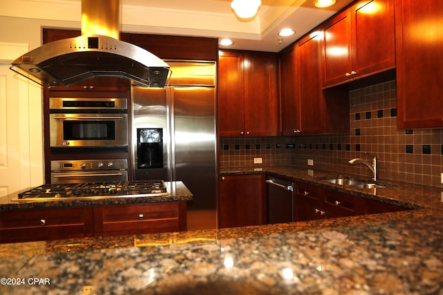 kitchen featuring sink, backsplash, stainless steel appliances, island exhaust hood, and dark stone counters