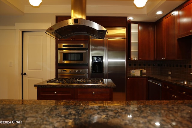 kitchen with tasteful backsplash, sink, dark stone counters, island exhaust hood, and stainless steel appliances