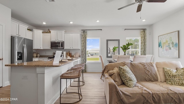 kitchen featuring white cabinetry, stainless steel appliances, dark stone countertops, light hardwood / wood-style floors, and a kitchen breakfast bar