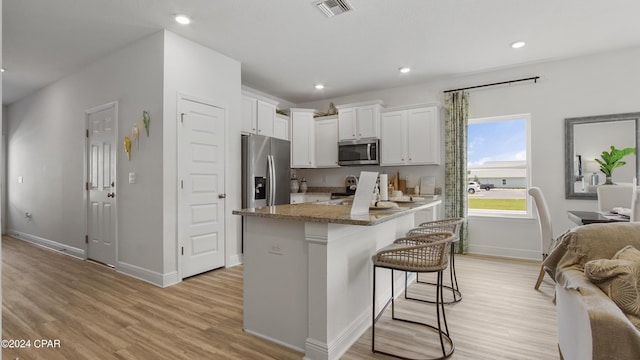 kitchen featuring a kitchen bar, appliances with stainless steel finishes, light wood-type flooring, stone counters, and white cabinets