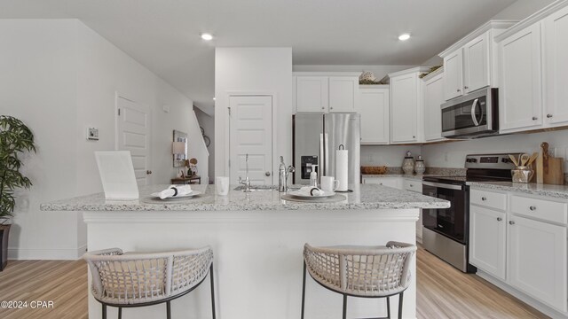 kitchen with a kitchen bar, white cabinetry, stainless steel appliances, and light hardwood / wood-style floors