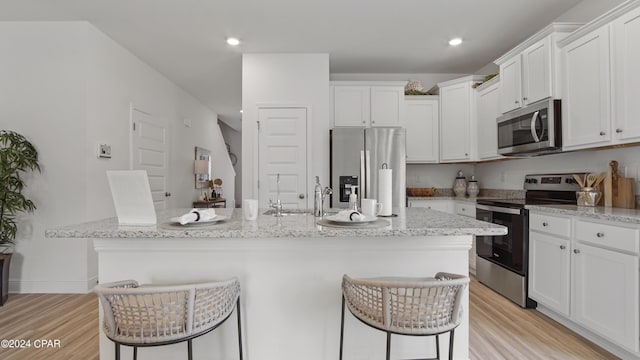 kitchen featuring light stone counters, a kitchen breakfast bar, a center island with sink, and stainless steel appliances