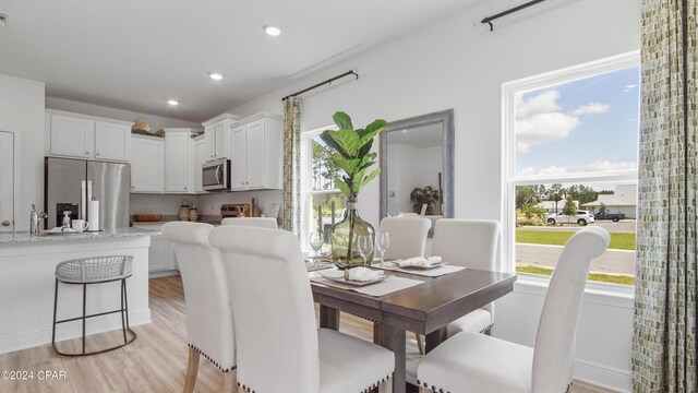 kitchen featuring a kitchen bar, appliances with stainless steel finishes, light hardwood / wood-style flooring, stone counters, and white cabinetry