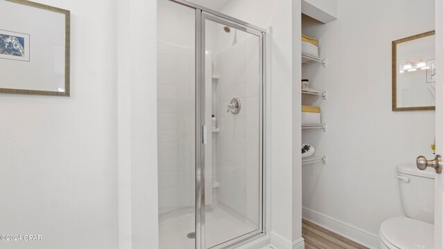 bathroom with hardwood / wood-style floors, toilet, and a shower with door