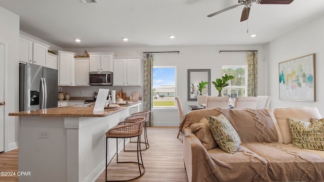 kitchen featuring light wood-type flooring, stainless steel appliances, white cabinetry, and a breakfast bar area