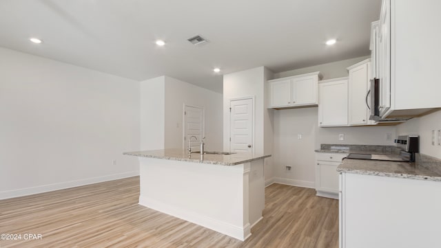 kitchen featuring light hardwood / wood-style floors, white cabinetry, a kitchen island with sink, and black stove