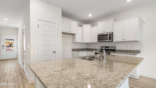 kitchen featuring stainless steel appliances, white cabinetry, sink, an island with sink, and light hardwood / wood-style flooring