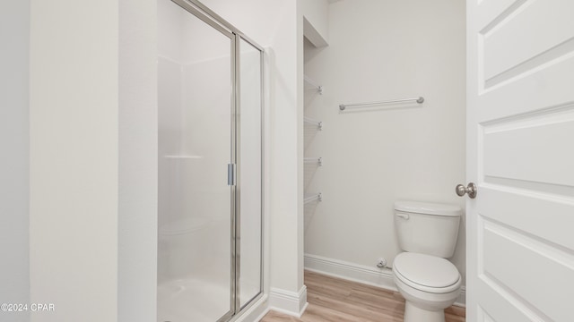 bathroom with hardwood / wood-style floors, toilet, and a shower with door