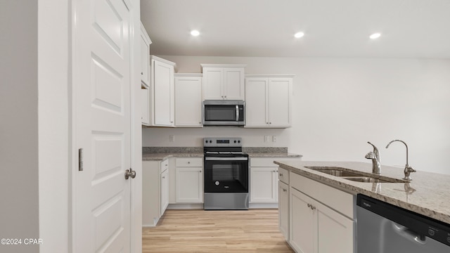 kitchen with stainless steel appliances, white cabinetry, sink, and light stone counters