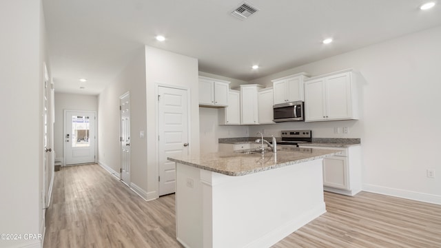 kitchen with light hardwood / wood-style floors, white cabinetry, appliances with stainless steel finishes, light stone countertops, and an island with sink