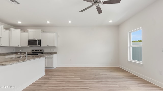 kitchen with light stone counters, stainless steel appliances, light wood-type flooring, sink, and white cabinets