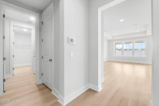 hallway with a tray ceiling and light wood-type flooring