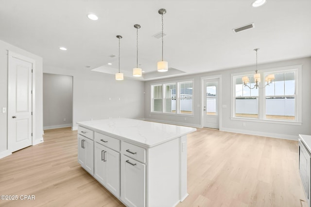 kitchen featuring white cabinetry, a center island, light wood-type flooring, a raised ceiling, and pendant lighting