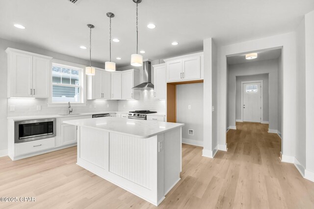 kitchen featuring wall chimney range hood, sink, white cabinetry, a kitchen island, and built in microwave