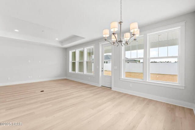 unfurnished dining area with a notable chandelier, a raised ceiling, a healthy amount of sunlight, and light wood-type flooring