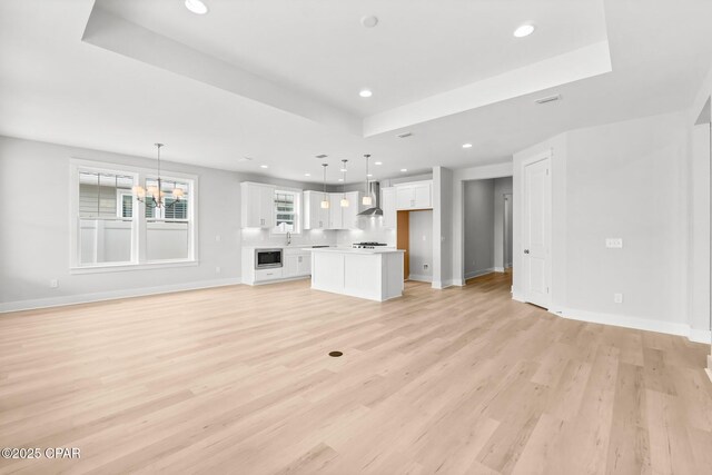 unfurnished living room featuring an inviting chandelier, a raised ceiling, and light wood-type flooring