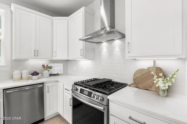 kitchen featuring stainless steel appliances, white cabinetry, light stone countertops, and wall chimney range hood