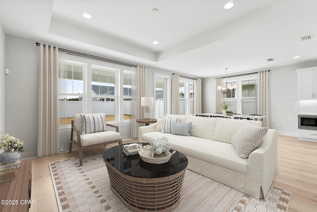 living room with a notable chandelier, a tray ceiling, and light hardwood / wood-style flooring