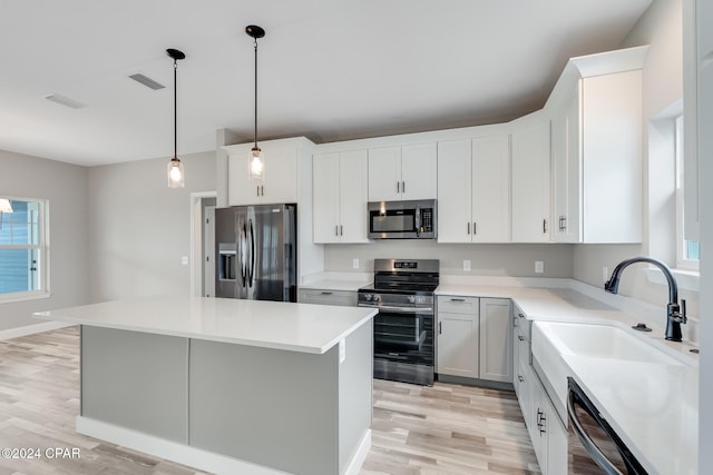 kitchen featuring stainless steel appliances, sink, decorative light fixtures, white cabinetry, and a kitchen island