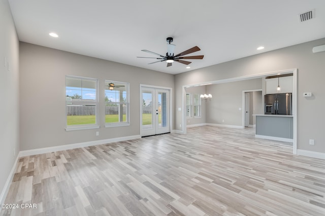 unfurnished living room featuring ceiling fan with notable chandelier, light hardwood / wood-style floors, and french doors