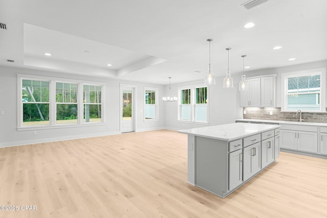 kitchen featuring pendant lighting, a tray ceiling, light stone countertops, a kitchen island, and light wood-type flooring