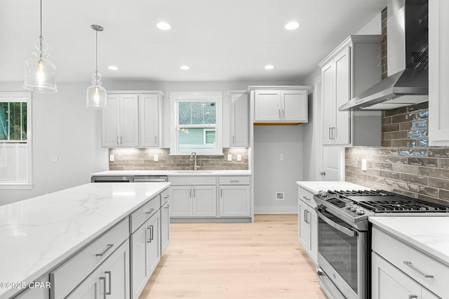 kitchen featuring sink, gas range, light stone counters, decorative light fixtures, and wall chimney range hood