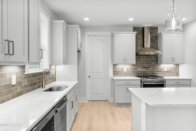 kitchen featuring appliances with stainless steel finishes, decorative light fixtures, sink, light stone countertops, and wall chimney exhaust hood