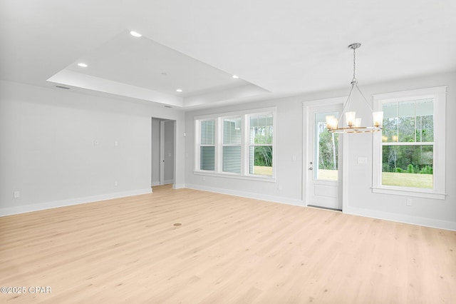 empty room featuring an inviting chandelier, light hardwood / wood-style floors, and a raised ceiling