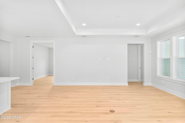 empty room with plenty of natural light, light hardwood / wood-style floors, and a raised ceiling