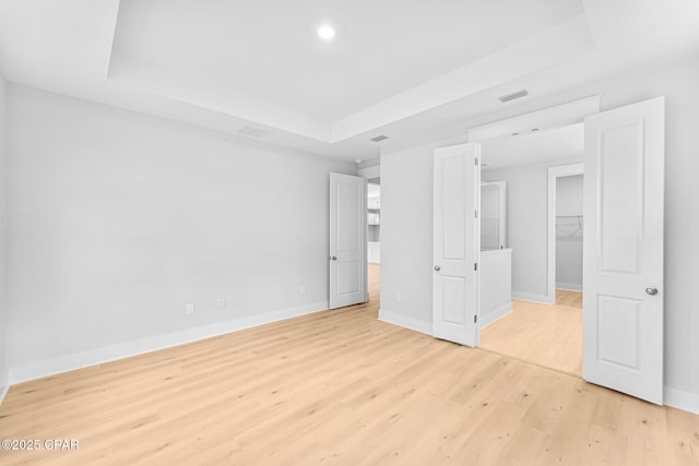 unfurnished bedroom featuring a closet, a tray ceiling, and light hardwood / wood-style flooring