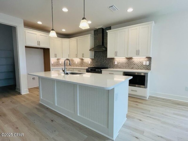 kitchen with wall oven, white cabinets, hanging light fixtures, and wall chimney range hood