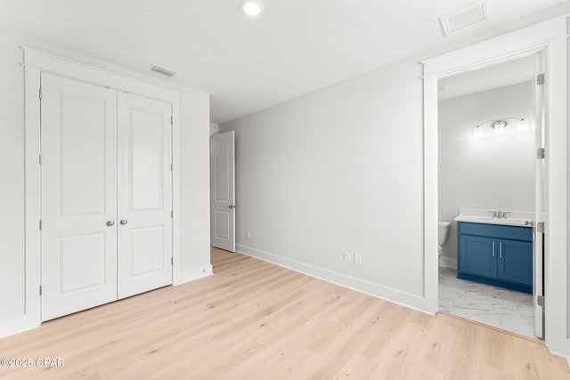 unfurnished bedroom featuring ensuite bathroom, sink, light wood-type flooring, and a closet