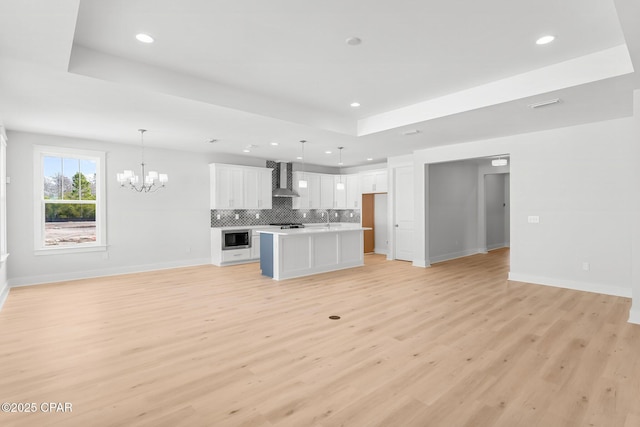 unfurnished living room with a raised ceiling, sink, an inviting chandelier, and light hardwood / wood-style flooring