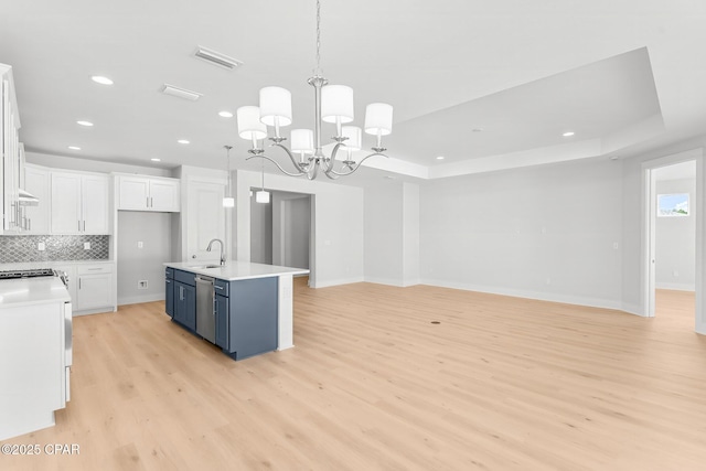 kitchen with blue cabinets, sink, white cabinets, hanging light fixtures, and a center island with sink