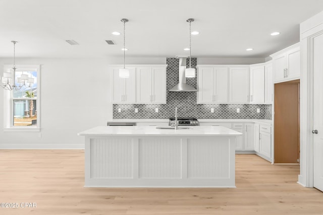 kitchen with wall chimney exhaust hood, sink, pendant lighting, a kitchen island with sink, and white cabinets